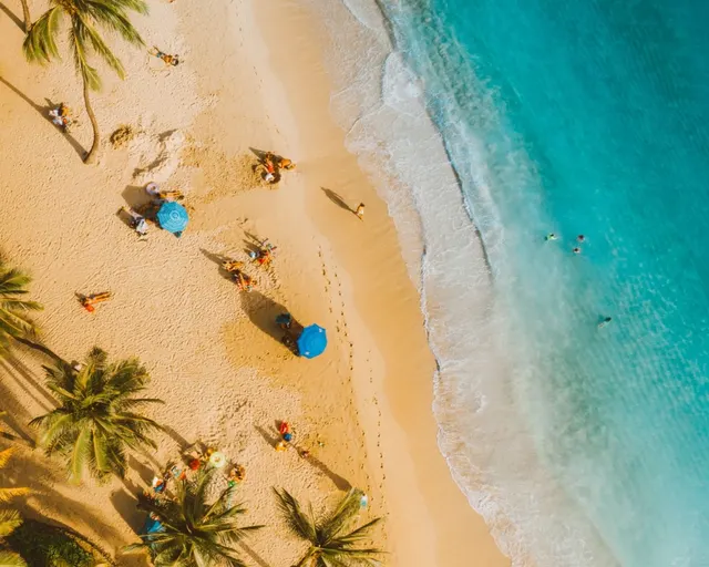 Vista aérea de una playa de arena dorada y agua turquesa con bañistas